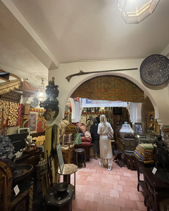 Cozy antique shop interior with wooden arch doorway, shelves filled with textiles and decor; two customers browse items near the back